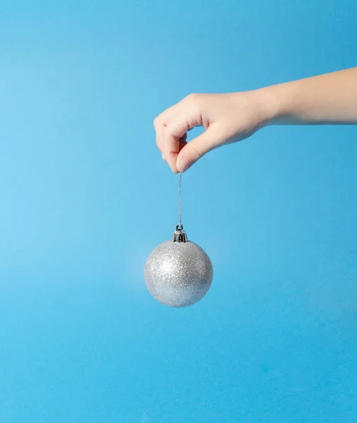 Elinde parıldayan gümüş bir Noel süsü. Minimum Yeni Yıl Sahnesi.