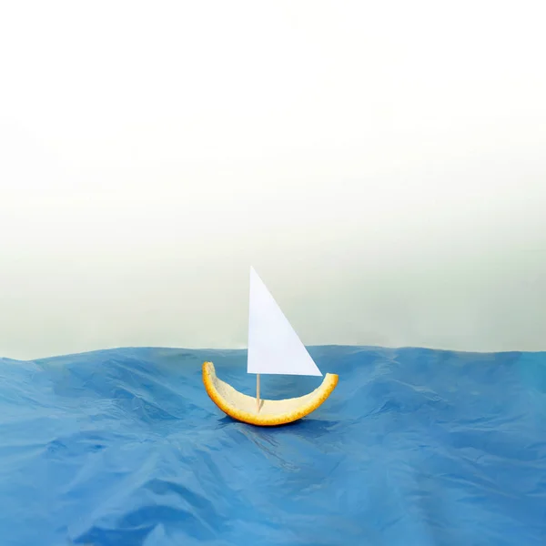 Yaz tatili planı portakal kabuğundan yapılmış küçük bir tekne, mavi su ve parlak bir arka plan. Yaratıcı asgari deniz kavramı.