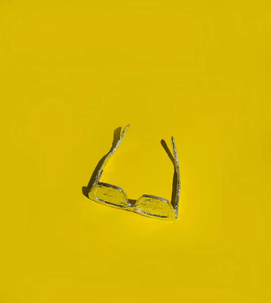 Sarı arka planda alüminyum folyoya sarılı güneş gözlükleri. Maksimum güneş koruması yaz fikri.