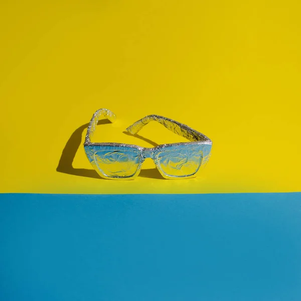 Sarı arka planda alüminyum folyoya sarılı güneş gözlükleri. Maksimum güneş koruması yaz fikri.