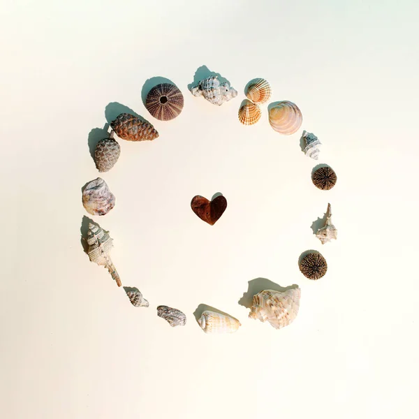 Ortasında kalp şeklinde bir yaprak olan deniz kabuklarından yapılmış bir daire. Bej arka planda asgari bir yaz fikri.