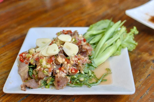 Baharatlı domuz etli Tayland salatası taze fesleğen yaprağı ve gümüş çatal saplanmış lahana ile yenir..