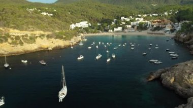 Cala Vedella plajının hava manzarası. Kıyıya yakın yelkenliler ve tekneler. İbiza adasındaki İHA görüntüleri.