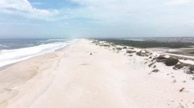 Portekiz sahilinde büyük kum tepeleri olan kocaman boş bir sahil. Paramotor sahilde uçuyor..