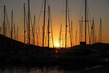 Portakal rengi günbatımında yat direkleri marinada duruyor.