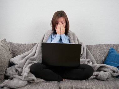 Yumuşak bir battaniyeye sarılı genç bir kadın evdeki kanepede oturuyor ve bir dizüstü bilgisayar kullanıyor. Sıkıcı kız..