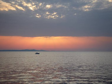 Hırvatistan 'ın Zadar kenti ve Adriyatik Denizi üzerindeki batan güneşin manzarası ünlü gezinti güvertesinden görüldüğü üzere küçük bir tekneyle.