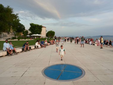 Zadar, Hırvatistan - 27 Temmuz 2021: Turist kalabalığı deniz orgu gezinti güvertesinde gün batımını bekliyor.