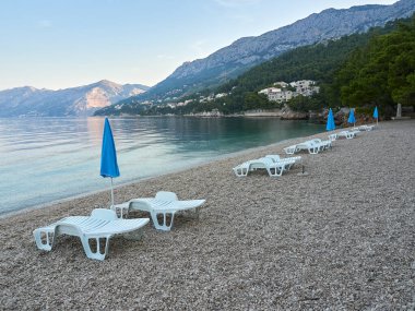 Hırvatistan 'ın Brela tatil beldesinde Punta Rata Plajı. Kumsaldaki boş güneş pansiyonları ve şemsiyeler. Güzel Adriyatik Denizi manzarası.