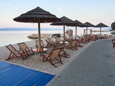 Baska Voda, Hırvatistan - 24 Temmuz 2021: Sahil beldesi Baska Voda 'da güneşlik ve şemsiyeli sahil barı. Deniz kenarında güzel, sessiz bir sabah.