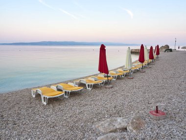 Baska Voda 'daki Ikovac plajında boş güneş pansiyonları ve şemsiye. Turistleri bekleyen bir sahil beldesi. Hırvat şehrinde Adriyatik 'te güzel sakin bir sabah