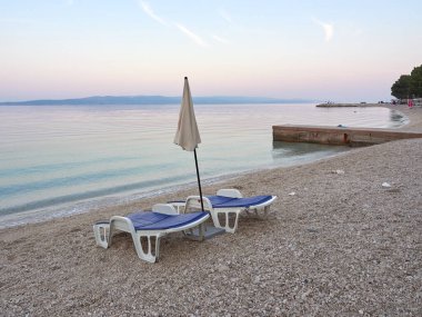 Baska Voda 'daki Podluka plajında boş güneş pansiyonları ve şemsiye. Turistleri bekleyen bir sahil beldesi. Hırvat şehrinde Adriyatik 'te güzel sakin bir sabah