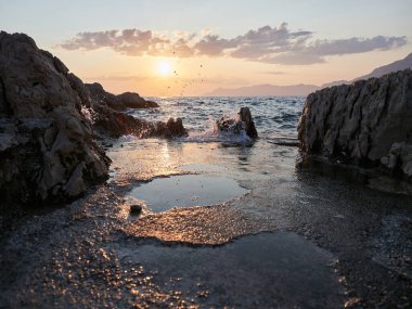 Adriyatik Denizi dalgalarının kayalara çarpması üzerine seçici bir odak noktası. Deniz kenarında gün batımı. Güzel Deniz Manzarası.
