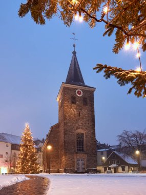 Velbert, Almanya - 17 Ocak 2021: Karla kaplı Eski Evanjelik Kilisesi ve ışıklı Noel ağaçları. Noel havası.