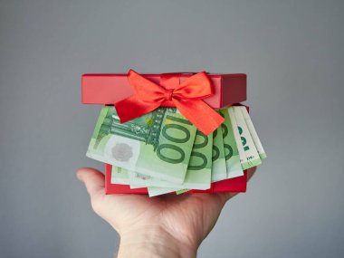 Parayla dolu kırmızı bir hediye kutusu. Avro banknotları elinde tutulan bir kutu. Parasal bir hediye..