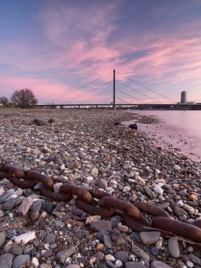 Düsseldorf 'taki Ren nehrinin kıyısındaki Oberkasseler köprüsünün manzarası. Güneşin doğuşunda güzel şehir manzarası