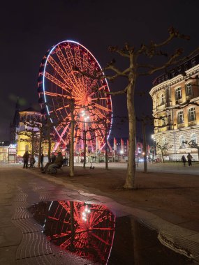 Düsseldorf, Almanya - 1 Ocak 2021: Dönme dolabın akşam manzarası güzel bir şekilde kırmızı ışıklarla aydınlatılmış, adı da Vison Çarkı. Su birikintisinde mimarinin yansımaları. Geceleyin gezinti.