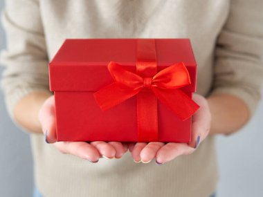 Kadın eli kırmızı bir hediye kutusu tutuyor. Kırmızı kurdeleli doğum günü ve Noel hediyesi. Bir kutuda hediye vermek. Hediye ve Noel zamanı..