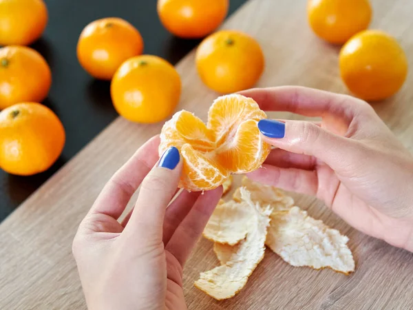 Mandarin soyuyorum. Dişi eller taze portakal meyvesini soyarlar. Meyveler masada yatıyor. Mandalina kabuğu.