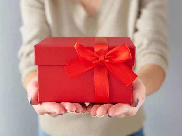 Kadın eli kırmızı bir hediye kutusu tutuyor. Kırmızı kurdeleli doğum günü ve Noel hediyesi. Bir kutuda hediye vermek. Hediye ve Noel zamanı..