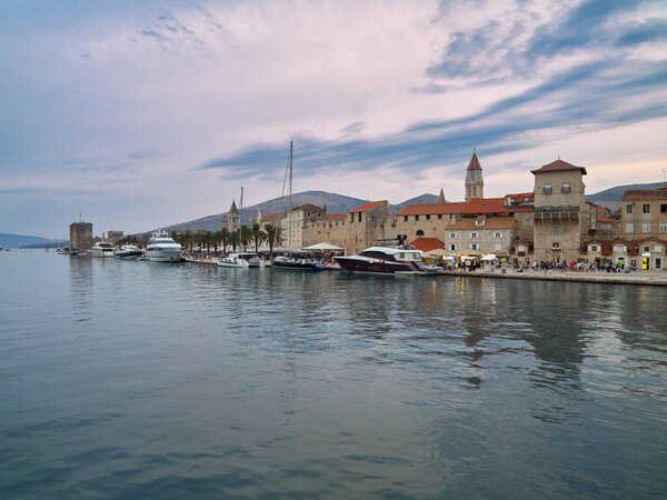 Трогир / Далмация / Хорватия 24 августа 2020 Причал для яхт класса люкс, прогулочная набережная с пальмами и исторический старый город Трогир. Вид на город после заката в голубой час.