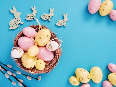 Sepette sarı ve pembe paskalya yumurtalarının düz kompozisyonu ve mavi arka planda paskalya tavşanları ve metin için boşluk.