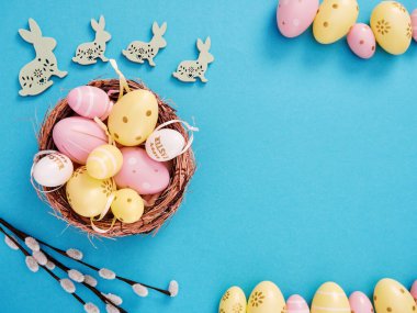 Sepette sarı ve pembe paskalya yumurtalarının düz kompozisyonu ve mavi arka planda paskalya tavşanları ve metin için boşluk.