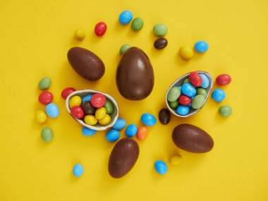 Düz kompozisyonda çikolatalı yumurtalar ve sarı arkaplanda renkli şekerler ve metin için yer vardı. Paskalya teması.
