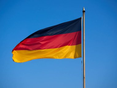 Direkte asılı Almanya bayrağı. Mavi gökyüzüne karşı rüzgarda dalgalanan bir bayrak..