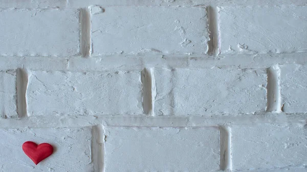 a red heart located in the lower left corner, on a light brick background, a place to copy