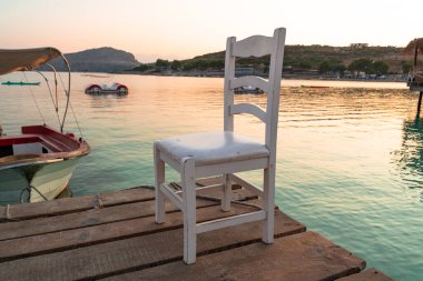 Sabah güneş doğarken turkuaz deniz suyunda kahverengi ahşap iskelede beyaz ahşap sandalye.