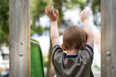 Çocuk kollarını kaldırır ve oyun parkındaki kaydırağın üzerinde kayar.