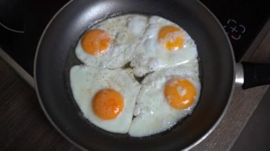 Tuz ve biberli dört yumurta aynı anda yağlı tavada ağır çekimde kızarıyor.