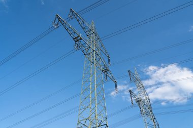 Mavi gökyüzünde yüksek voltajlı elektrik hatları olan büyük elektrik direklerinin alt görünümü