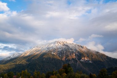 Karlı bir zirvesi olan dağ ve bir sonbahar gününde gökyüzünde büyük beyaz bulutlar