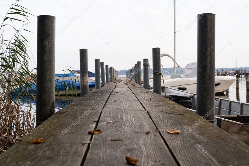 Wooden pier in autumn morning with tied up boats on the sides