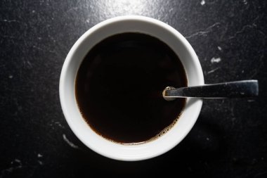 Siyah mutfak tezgahında siyah kahve ve beyaz desenli beyaz fincan.