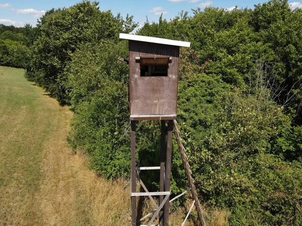Hunting tower with a wooden ladder in the field and with bushes in the background