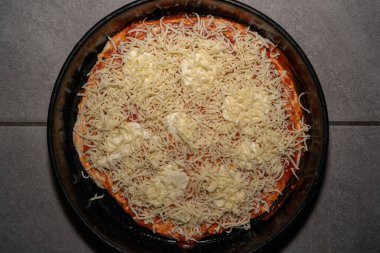 Domates soslu, mozarellalı ve rendelenmiş peynirli fırında pişmemiş pizza.