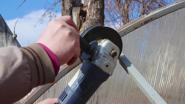Hands with an angle grinder cut a rusty old metal greenhouse. — Stock Video