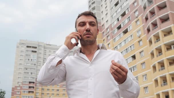Un homme d'affaires en chemise blanche parle émotionnellement au téléphone. — Video