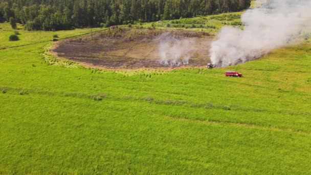 Una sezione bruciata del campo sta fumando, un pompiere sta guidando. — Video Stock