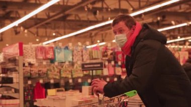 Yakın plan genç adam süpermarketten satın alıyor, yüzünde bir maskeyle.