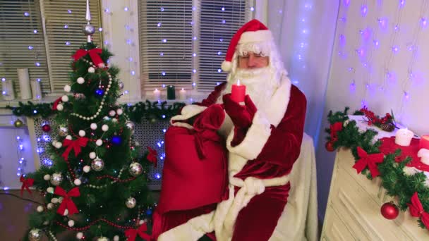 Moderní Santa Claus s pytlem se dívá na zarůstající červenou svíčku. — Stock video