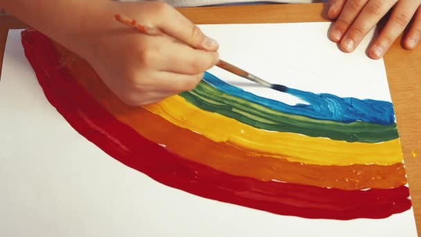 Ένα παιδικό χέρι σχεδιάζει ένα όμορφο ουράνιο τόξο με χρωματιστά χρώματα σε ένα φύλλο. — Αρχείο Βίντεο
