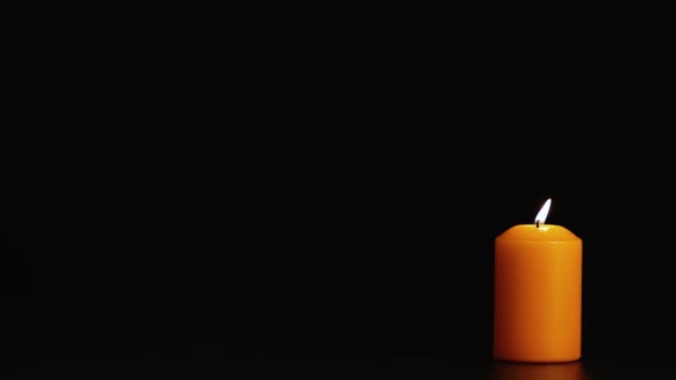 One yellow burning candle on a black background in the dark. Copy space. — Stock Video