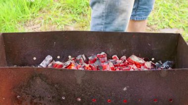 Adam ızgarada yemek pişirmek için kızgın kömürleri yelliyor..