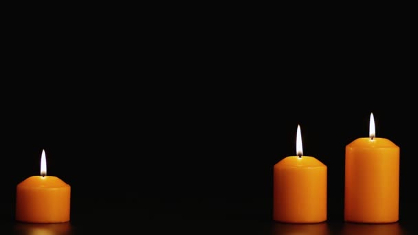 Three yellow burning candles on a black background. Copy space. — Stock Video