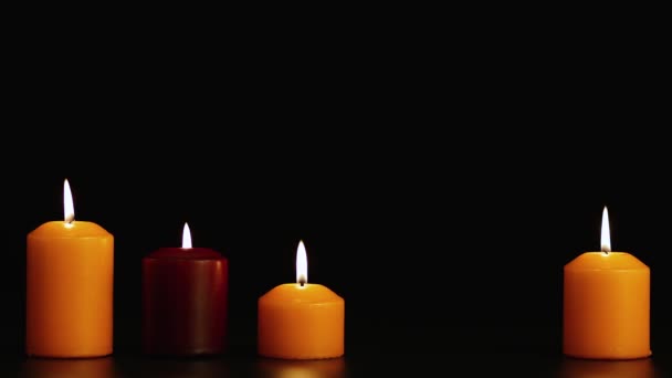 Quatro lindamente queimando velas diferentes em um fundo preto. Espaço de cópia. — Vídeo de Stock