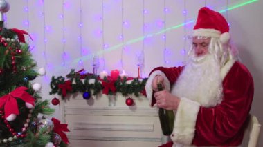 Noel Baba şampanyayı açar ve kameraya bakar..